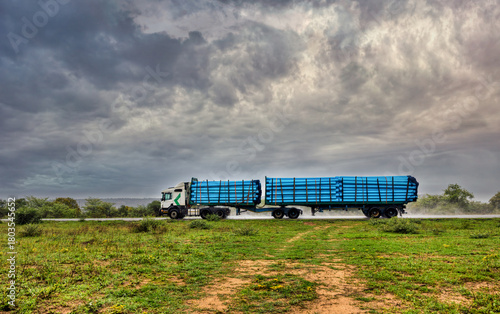 Fotografia commercial truck hauling a large quantity of plastic pipes on an open road in the heavy rain storm, flatbed trailer configuration carrying concrete pipes