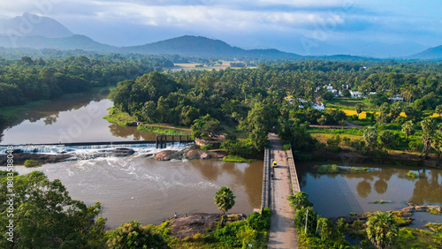 Aerial view of Attala Bridge and Cheramangalam check dam in Palakkad, Kerala, India, with river waters, lush green landscapes, coconut groves, and distant Western Ghats hills under a cloudy blue sky.
