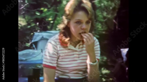 Bored teenage girl portrait at countryside camp on summer vacation. Teenage apathy, melancholy. Teen angst. Summer on bench boredom in nature. Old film. Archival retro 1960s. Vintage archive.