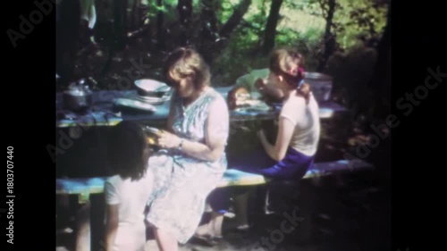 Family picnic in countryside outside city. Children, mother sharing meal together. Relaxation at picnic table outdoors in forest nature. Simple joys. Old film. Archival retro 1960s. Vintage archive