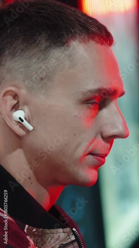 vertical close-up slowmo of a mans putting earphones in the ears, streetlights at night. The background is blurred creating a cinematic effect