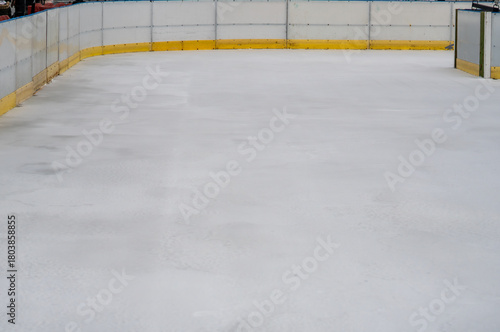 Empty ice rink with yellow boards in a winter urban setting, prepared for skating during seasonal holiday attractions