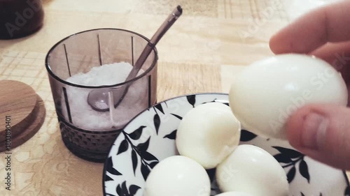 A person eating boiled chicken eggs. Hands peeling a boiled egg on a kitchen counter, oranges in the background, homecooked meal concept, fresh food preparation. Many eggs on the table.