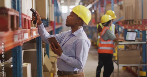 Inspecting warehouse supervisor wearing yellow hard hat scanning with barcode scanner and tablet