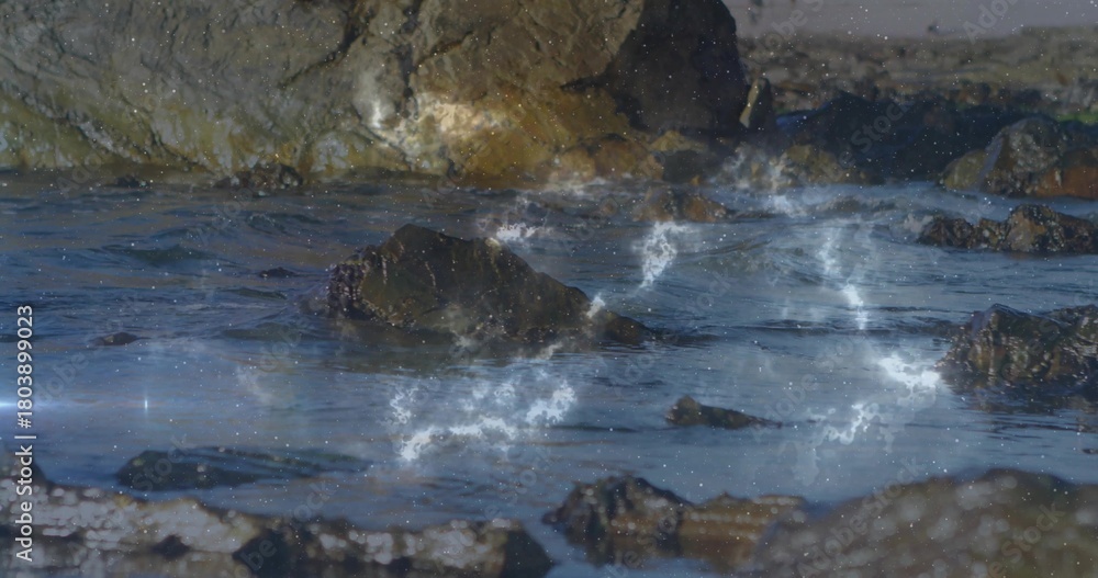 Obraz premium Glistening dark boulder cluster catching low sun at coastal shore, with tide pools, nebula