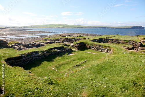 Ruins of the Brough of Birsay in Orkney, a ancient historic norse Viking settlement with weathered stone foundations set against rugged cliffs and bright blue coastal skies.