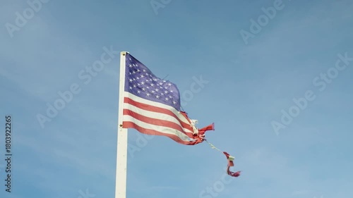 Close-up of a tattered American flag fluttering in the wind against blue sky symbolizing hardship and endurance. Symbols. Low angle view.