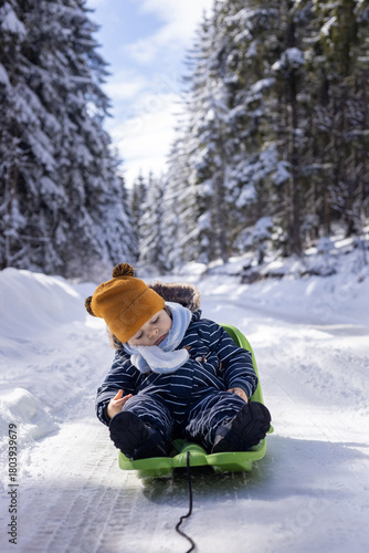Child sleeping on sled in snowy winter forest