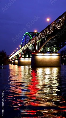 Illuminated bridge with holiday lights reflecting on water at night  