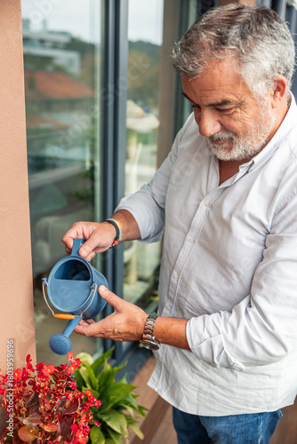 Senior man caring for balcony plants with watering can