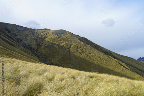 Danseys Pass Kakanui Range tussock-covered high country mountains in springtime under a blue cloudy sky. Waitaki and Central Otago in the South Island of New Zealand.