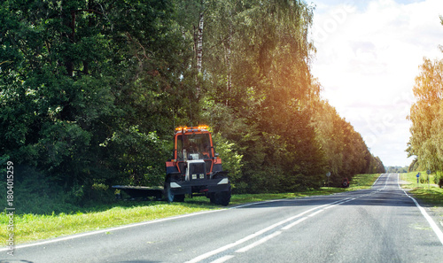 A special tractor with a mower for mowing grass on the side of the road against the background of a forest, industry. Copy space for text