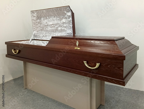 Matte brown wood coffin with white satin upholstery, open lid, and brass handles, displayed on stand. Elite Grob manufactures coffins in Kurganinsk