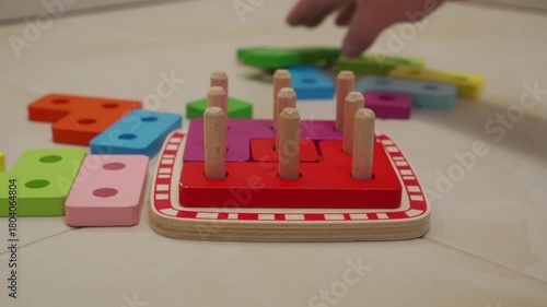 A hand slides a wooden shape-sorting puzzle into place on a hard tile floor. The wood drags across the floor, producing a short, low scrape.