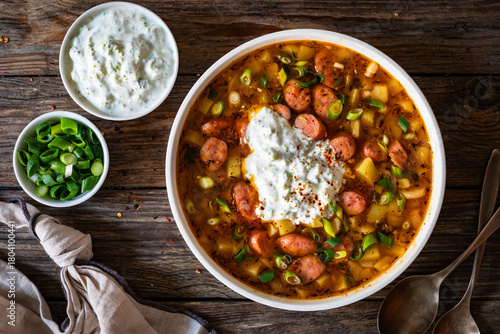 Potato soup with sausage and yogurt on wooden table. Top view