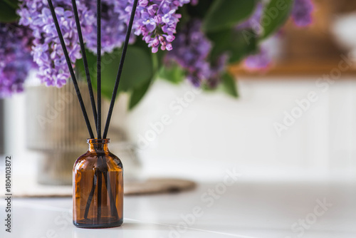 Aromatherapy, cozy atmosphere, comfort and relaxation. The aroma diffuser. Lilac-scented spring perfumes for the home in a glass bottle with chopsticks as an air freshener in the house.