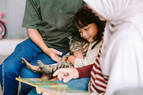 Young Girl Cuddles Pet Cat While Family Reads Book