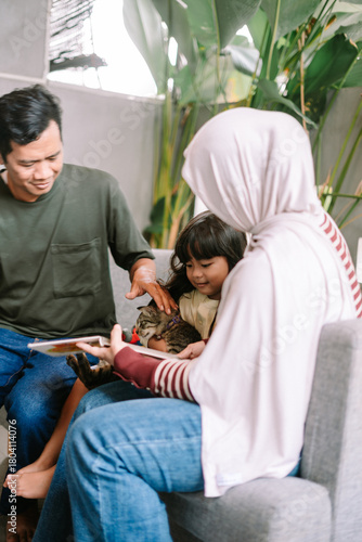 Happy Muslim Family Bonding with Pet Cat While Reading Together