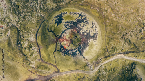 Aerial view of a volcanic crater with a vibrant red center surrounded by dark lava flows and green mossy terrain, Akureyri, Rangarbing ytra, Iceland.