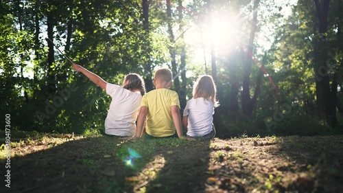 Kid sits with friend on grass kid and friend sit side by side near tree line backlight sunlight filters through forest canopy summer nature mood quiet play soft shadow pattern on ground warm bond link