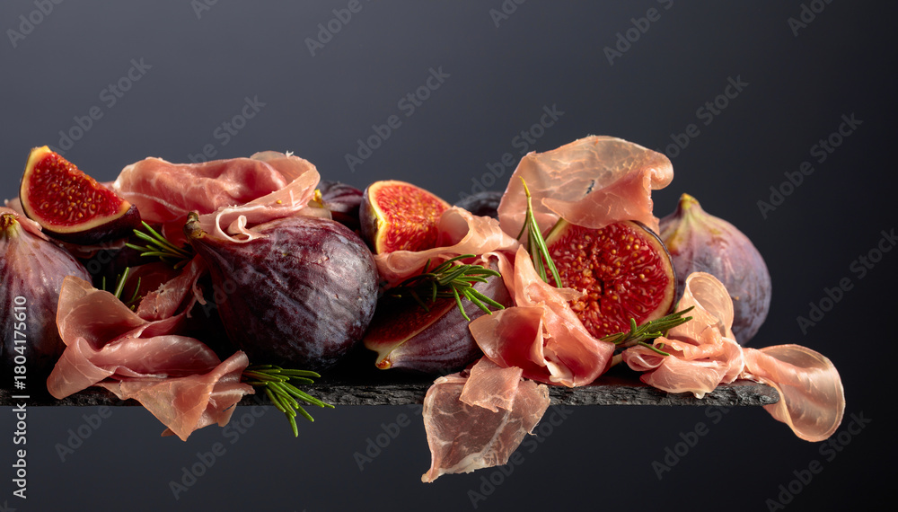 Fototapeta premium Prosciutto with rosemary and fig fruit on a black background.