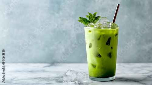 A glass of iced matcha latte, ice cubes in the drink, mint leaves on top