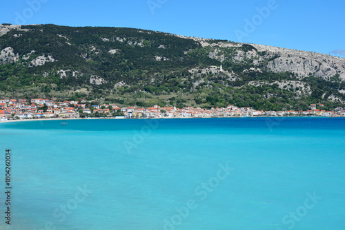 Fototapeta Naklejka Na Ścianę i Meble -  The picturesque town of Baska on Krk Island is nestled along a tranquil turquoise bay, backed by green and rocky hills under a clear blue sky