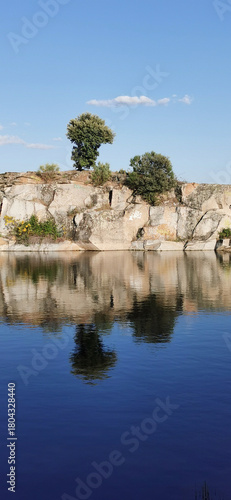 Calm lakeside view on a clear day with gentle ripples reflecting surrounding rocks and grassy shore