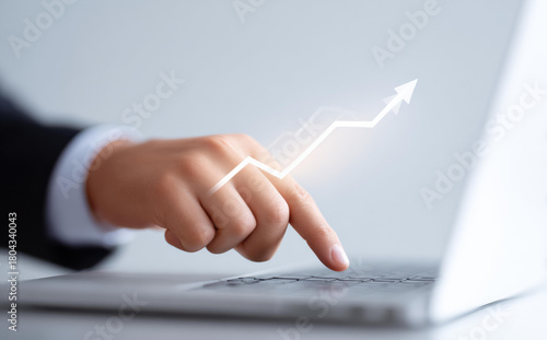 Optimistic businessman shows business growth and success with glowing arrow chart. His hand on laptop represents finance, investment, stock market, and technology progress