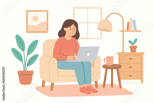 Young woman working on a laptop while sitting comfortably in a chair at home with a mug of coffee