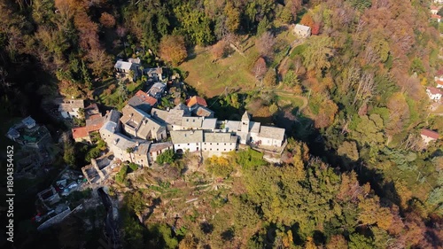 Aerial view of Carmine Superiore, a village with tightly packed stone buildings nestled into the mountainside surrounded by colorful autumn trees, Carmine Superiore, Piedmont, Italy.