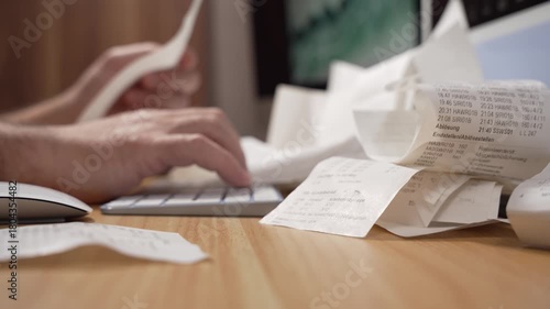 A man holds receipts above the keyboard while entering numbers on a computer in this clip. The video captures manual expense logging and tax preparation.