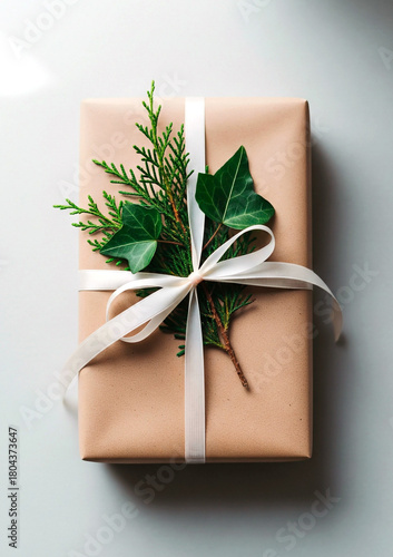 Elegant gift box wrapped in kraft paper with a white bow and fresh green foliage, exuding holiday charm in a refined festive photographic still life composition.