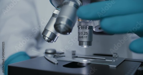 Detailed macro of gloved hands adjusting laboratory microscope for analysis