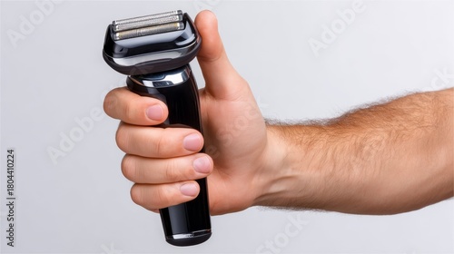 A close-up of a male hand firmly holding a sleek black electric shaver against a light gray background, showcasing the product's modern design