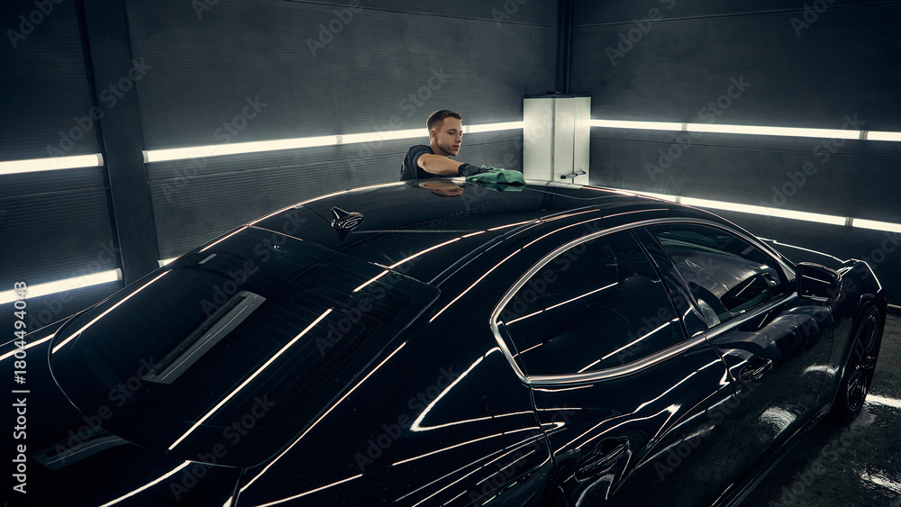 Naklejka premium Detailer polishing car roof with green microfiber cloth in detailing studio. Concept of quality care, precision workflow, and maintenance professionalism for auto service.