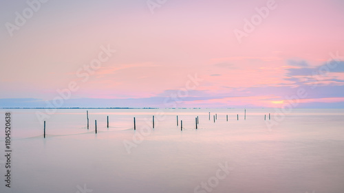 Vibrant sunset illuminates tranquil sea with leading lines of poles.