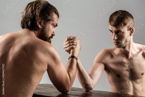 Two man's hands clasped arm wrestling, strong and weak, unequal match. Heavily muscled bearded man arm wrestling a puny weak man. Arms wrestling thin hand, big strong arm