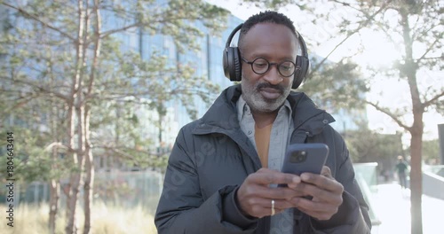 Man using Smartphone and wearing Headphones Walking in City