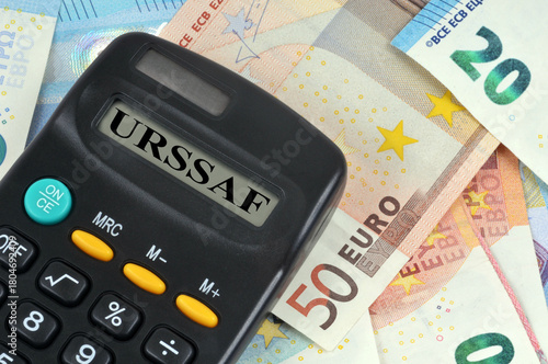 Concept de prélèvement URSSAF avec une calculatrice en gros plan et un fond de billets de banque en euro