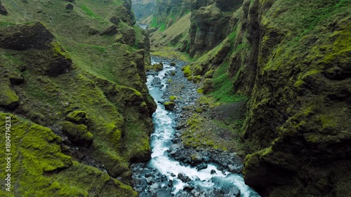 Aerial landscape of Mulagljufur Canyon and mossy cliffs. Drone flight above Iceland’s dramatic canyon, where bright green walls and a winding river shape a rugged natural scene.