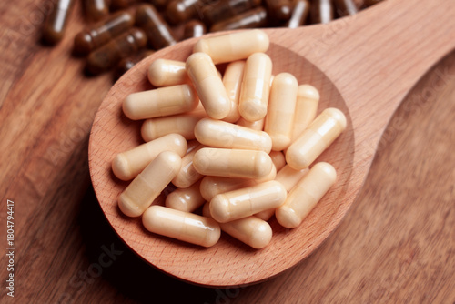 Beige capsules in wooden spoon on table with scattered brown pills
