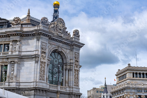 The grand stone facade of the Banco de España in Madrid shows detailed carvings, tall arched windows, and a golden dome crowning a corner tower with refined detailing