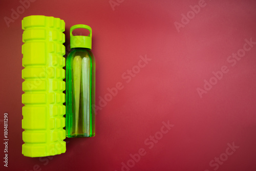 Vibrant green foam roller alongside a clear water bottle on a bold red background, highlighting essential fitness tools for health enthusiasts and workout sessions