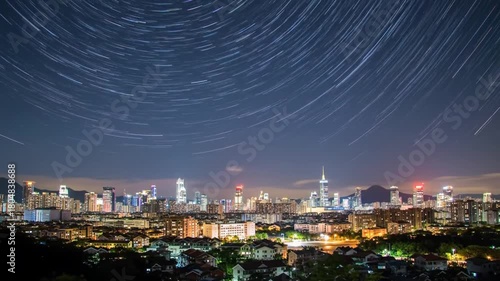 Stunning long-exposure photograph of circular star trails above a glowing urban cityscape at night.