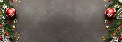 Long wide banner with fir tree branches, bright red balls and golden decorations on dark stone background with copy space for your design top view. Christmas and New Year festive banner.