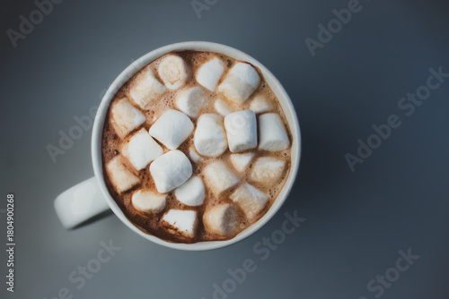 A warm mug of rich, creamy hot chocolate topped with a generous layer of fluffy marshmallows isolated on a table surface. high angle perspective with copy space flat lay background