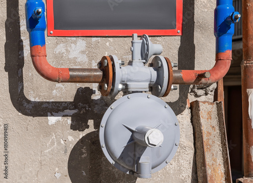 Gas piping system featuring a pressure regulator, valves, and rusty pipes on an old building wall