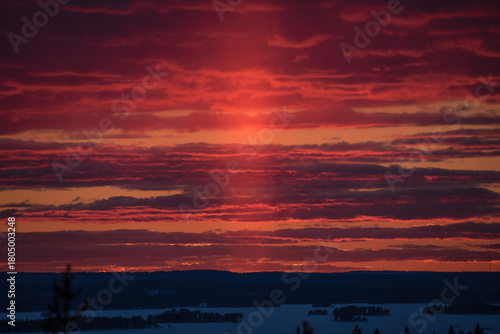 Sunset colours in the clouded sky over forested lake landscape in winter in Finland
