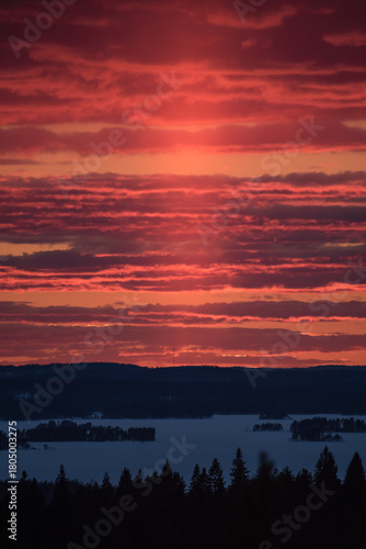 Sunset colours in the clouded sky over forested lake landscape in winter in Finland